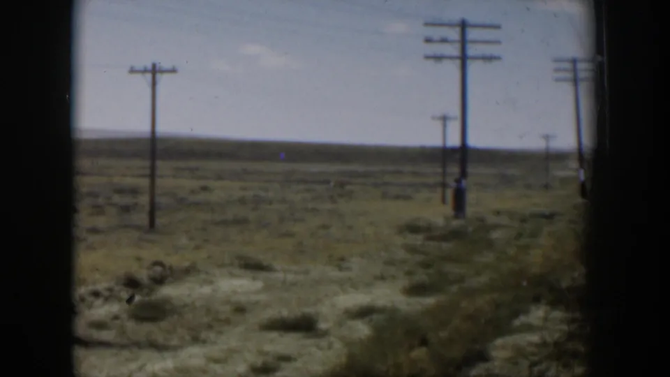 Wyoming 1951 home-movie frame showing utility poles, open scrubland, and a distant horizon from a moving vehicle.