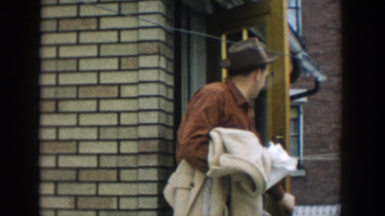 Man in a brown hat turns his head near a yellow doorway with brick walls behind him.