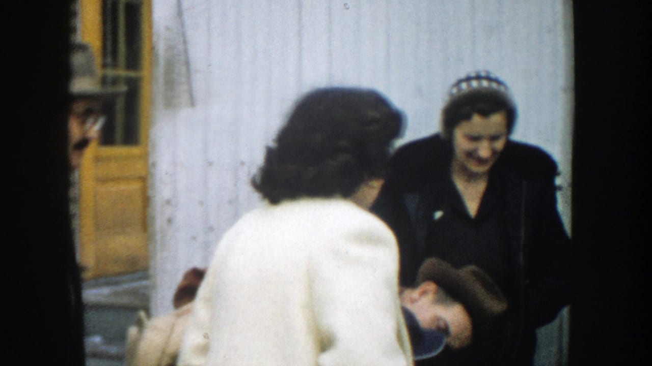 A woman in a dark coat smiles while others lean in during an outdoor greeting.