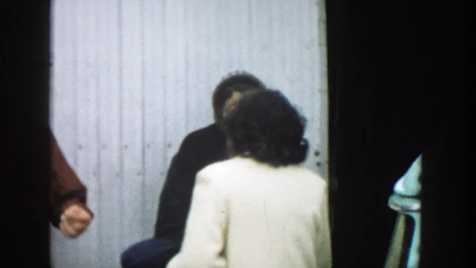 1957 Michigan frame showing women in light and dark coats near a doorway, with a man partly visible at the edge of the group.