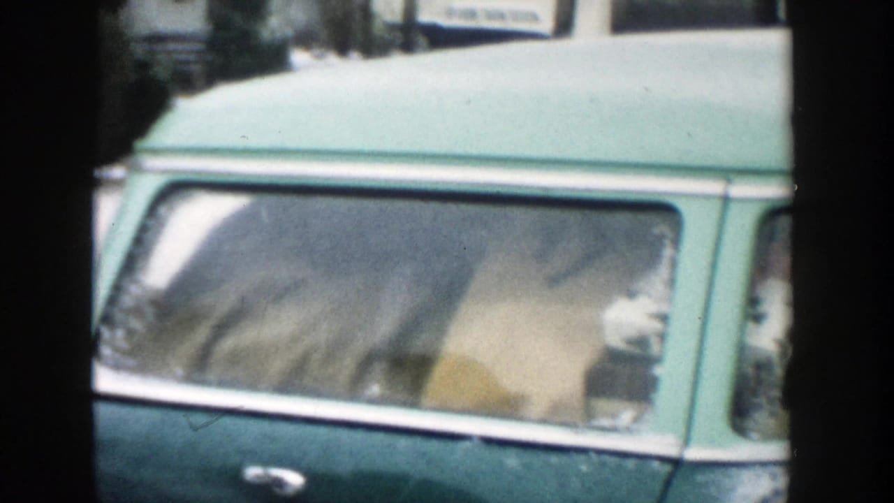 1957 Michigan home-movie frame showing a green station wagon with a packed interior on a residential street.