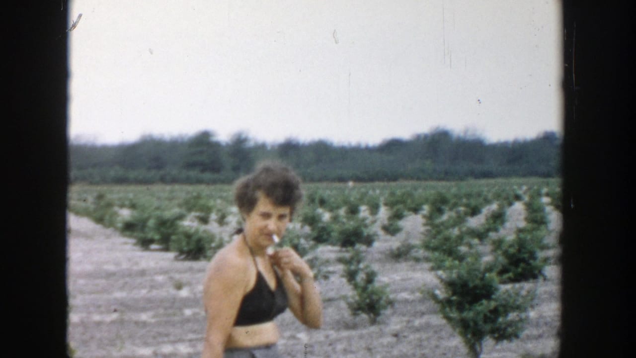 Woman in a black halter top holds a cigarette while standing in crop rows.