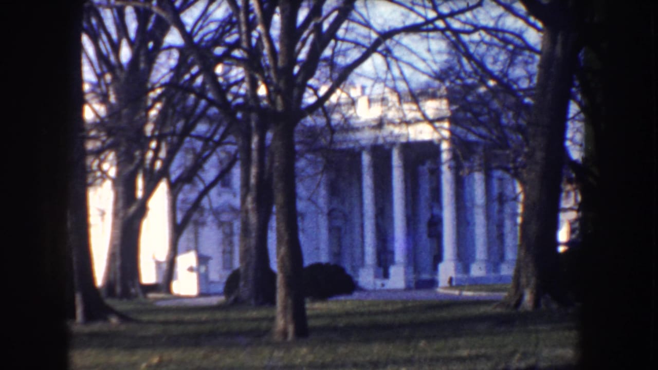 White House exterior in Washington, D.C., seen through leafless trees on blue-shifted 8mm home-movie footage from circa 1960.