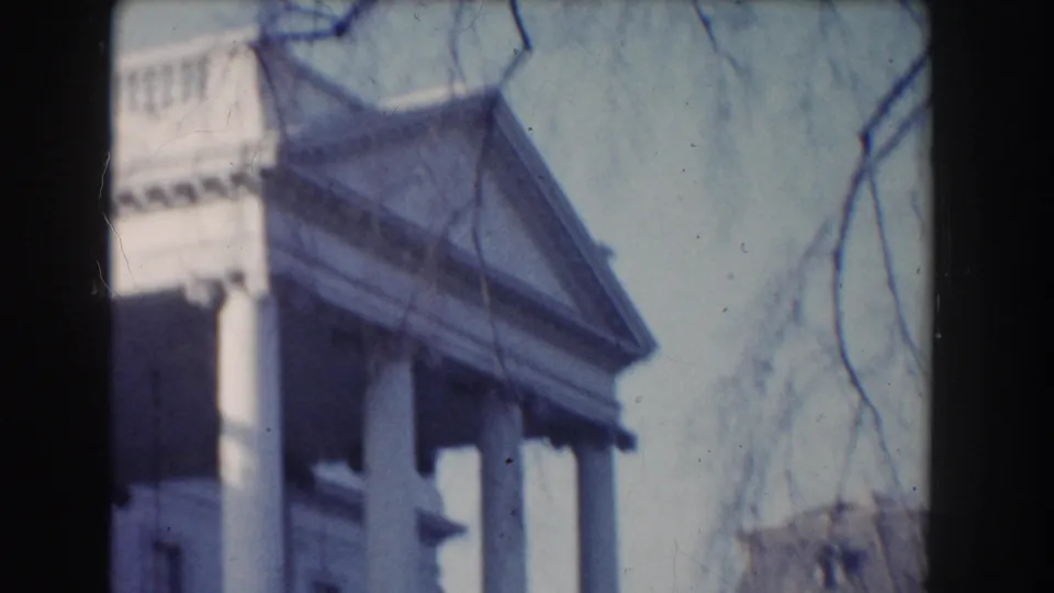 A tilted home-movie view shows the White House portico, columns, roofline, and bare tree branches in Washington, DC.
