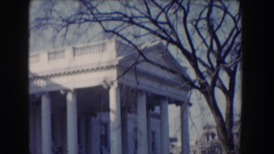 The White House portico appears behind bare tree branches, with columns and upper facade details visible in 8mm color footage.