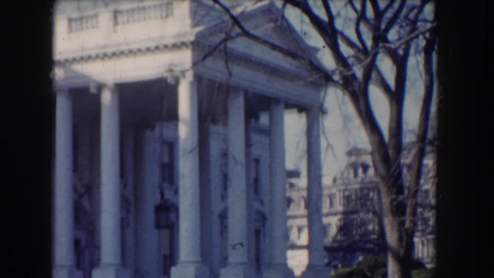 1960 8mm view of the White House facade in Washington, DC, with columns, bare branches, and soft home-movie focus.
