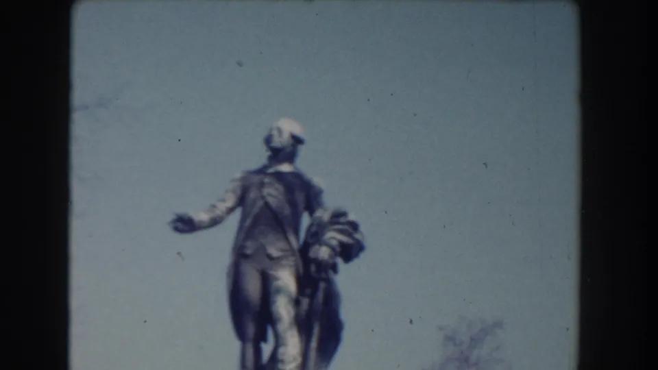 Washington, DC public statue viewed from behind on 8mm film, with a standing figure and smaller adjacent figure against open sky.