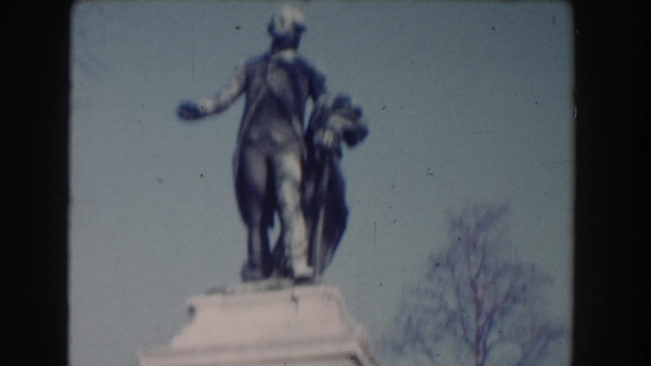 Lafayette statue on a pedestal against pale sky and bare trees.