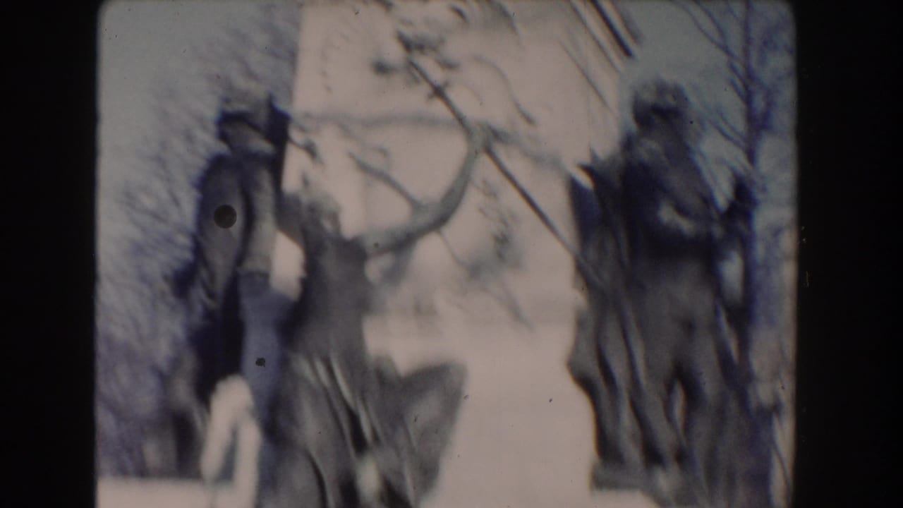 Soft 8mm view of sculptural figures around the Lafayette monument, with leafless branches crossing the background.