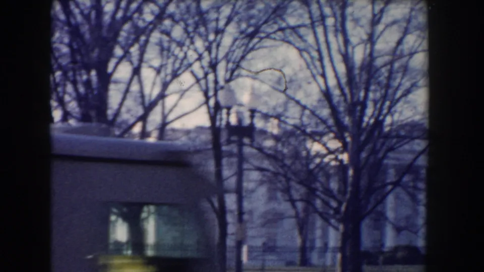 Handheld Lafayette Square view with a fence, bare trees, and a nearby building seen in cool-toned 8mm color.
