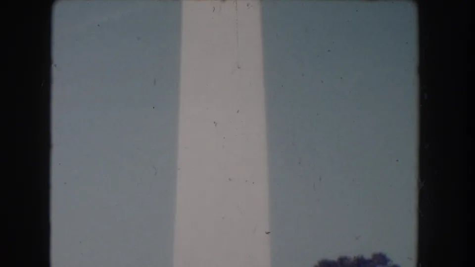 1960 Washington, D.C. home-movie frame with the monument shaft centered and treetops low at the right.