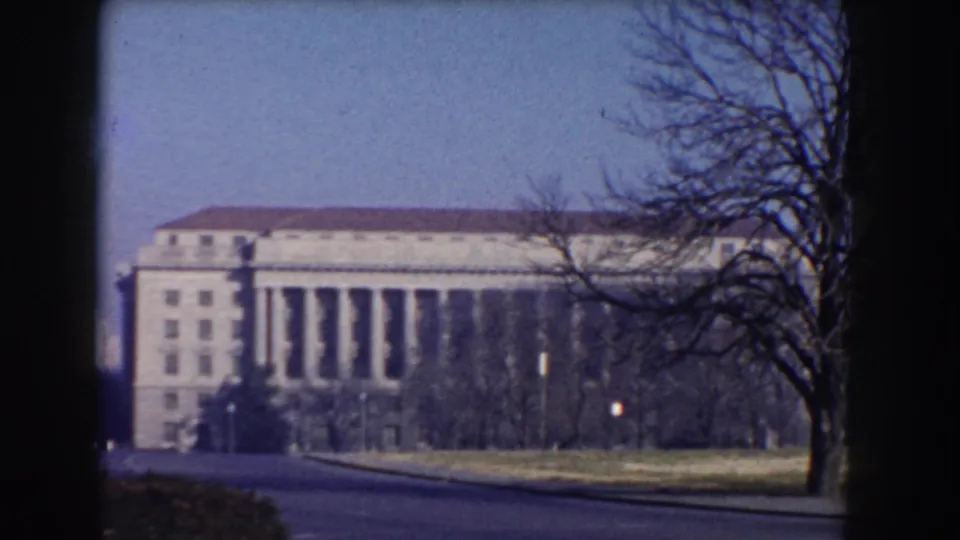 A Washington DC street-level view from 1960 shows a large classical building with columns, bare trees, roadway, and lawn.