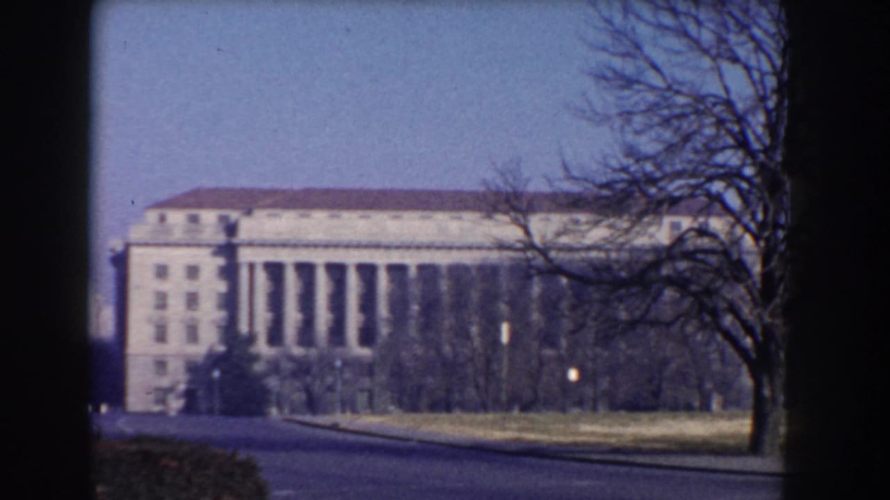 Neoclassical buildings seen across a road through bare trees in Washington DC.