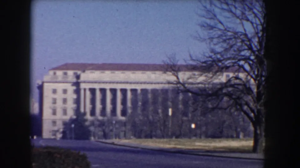 1960 8mm view of Washington DC federal-style buildings framed by winter trees and a dark foreground edge.