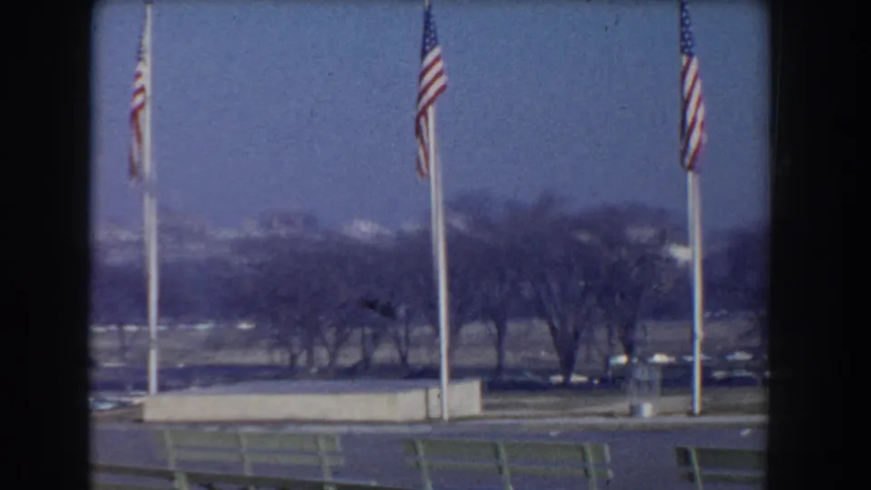 1960 Washington, DC view from the Mall area with flagpoles, bare trees, parked cars, and distant buildings under a blue sky.
