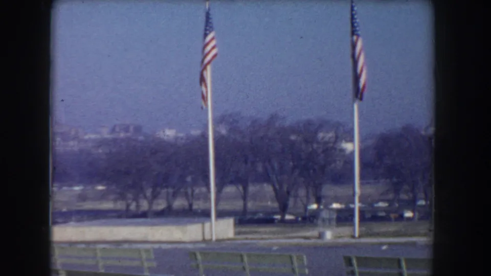Washington, DC 1960 8mm frame with American flags in the foreground and the Mall landscape extending toward trees and buildings.