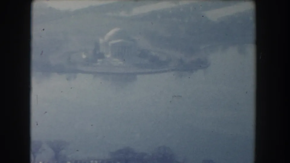 Soft 8mm frame from Washington, D.C. showing a hazy view across water toward a domed monument-like structure and shoreline trees.