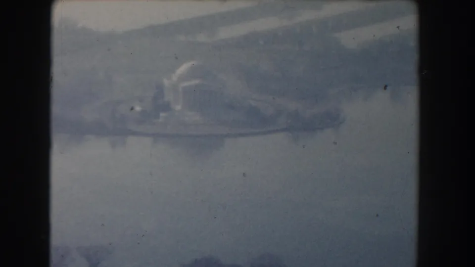 Hazy 1960 Washington, DC aerial frame showing water, shoreline, and distant urban forms through soft blue 8mm film texture.