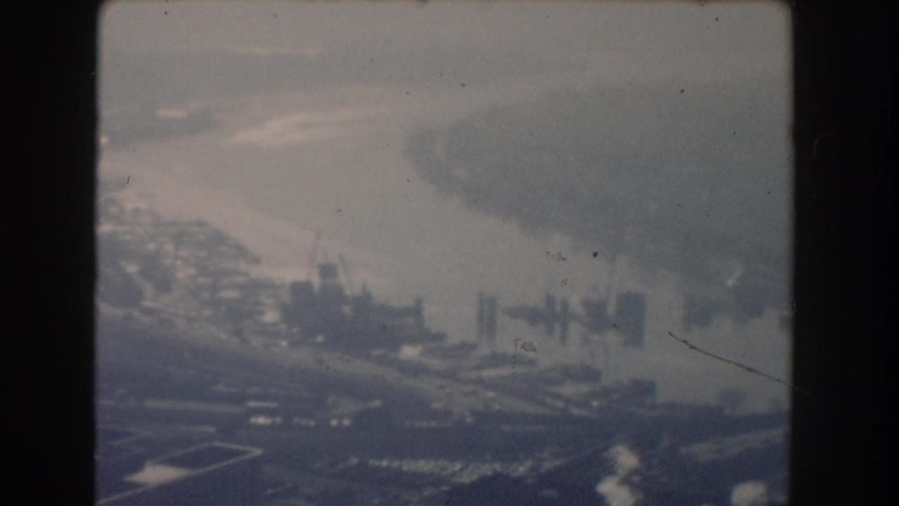 Aerial waterfront view with docks, buildings, river, and hazy shoreline.