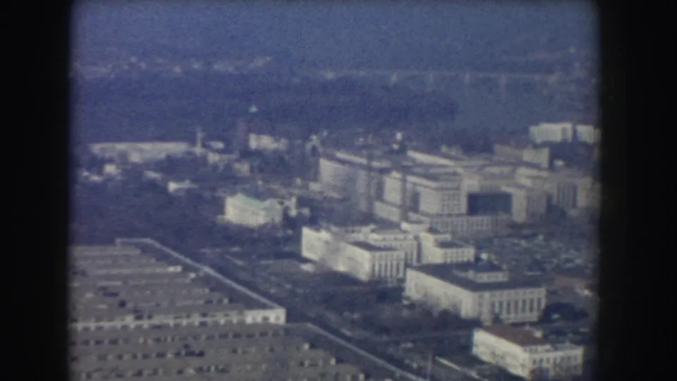 1960 aerial home-movie view over Washington, DC government buildings, softened by haze and framed by dark window edges.