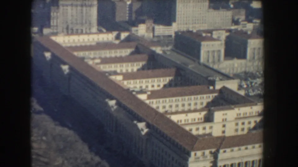 1960 aerial home-movie frame over Washington, DC showing a long federal-style building with red roofs and nearby office blocks.