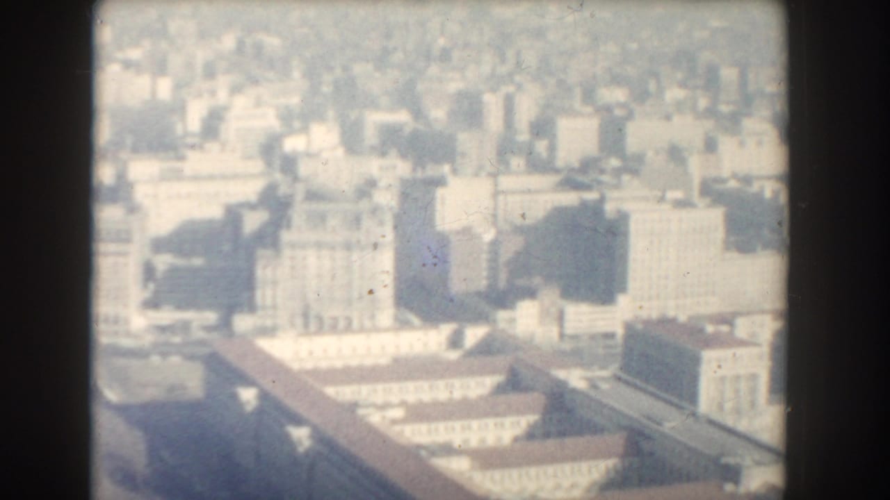 Soft elevated view of dense city buildings through a dark film-frame border.