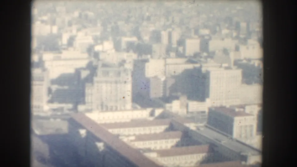 1960 Washington, DC aerial-style view of dense downtown buildings, rooftops, and pale civic structures in soft 8mm focus.