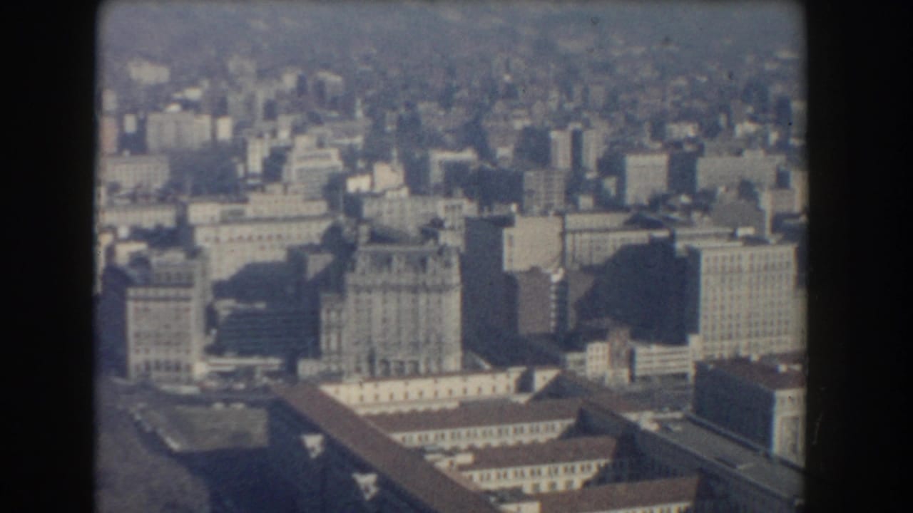 Elevated cityscape with tall buildings, rooftops, and a hazy skyline.