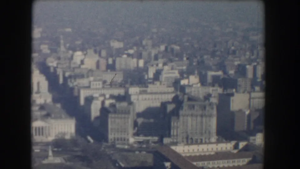 Elevated Washington, DC view with dense buildings, broad avenues, and a pale columned structure visible near the lower left.