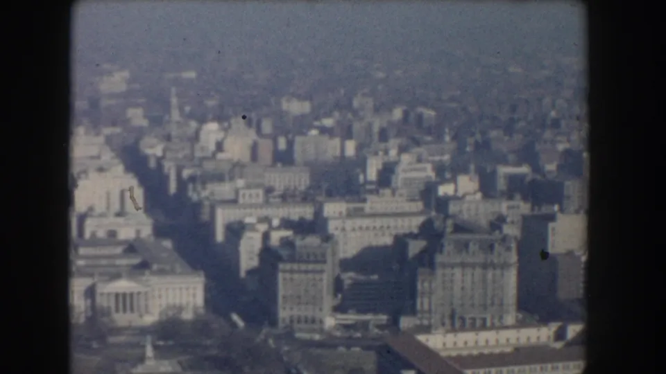 Soft 8mm frame of Washington, DC from above, with mid-century buildings, shadowed streets, rooftops, and city haze.