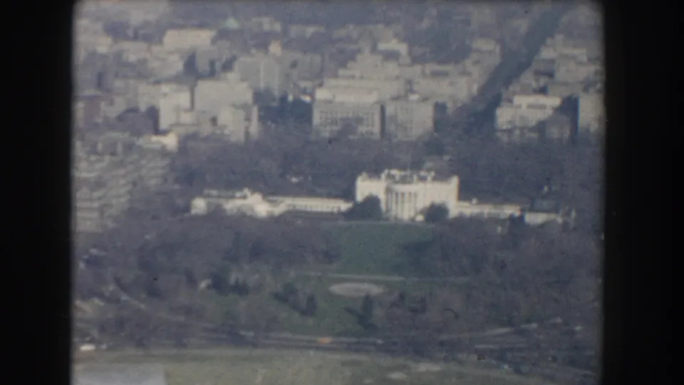 1960 aerial 8mm view across the White House grounds, framed by parkland, roads, and central Washington buildings.