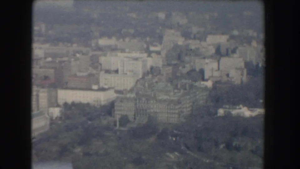 1960 Washington, DC aerial frame showing a castle-like stone building surrounded by trees, paths, and nearby city blocks.