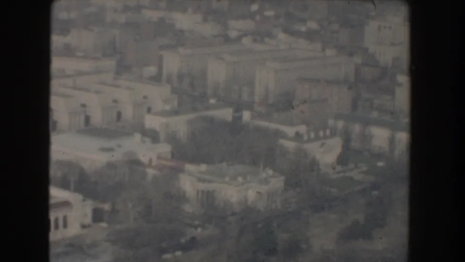 1960 8mm aerial view across Washington DC with federal-style buildings, rooftops, roads, and leafless trees in soft focus.