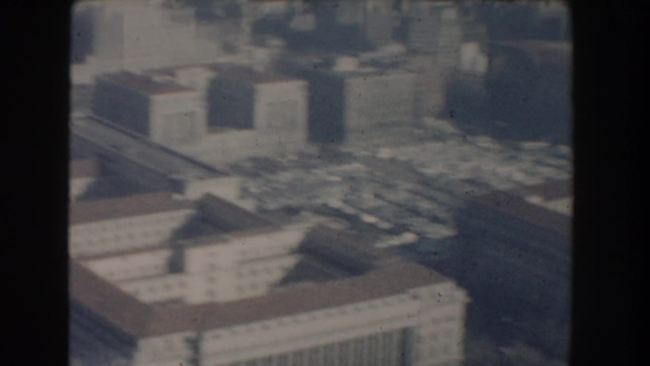 1960 Washington, DC aerial home-movie frame showing large government-style buildings, rooftops, streets, and haze.