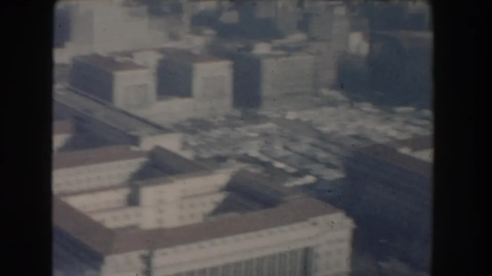 1960 Washington, DC aerial home-movie frame showing large government-style buildings, rooftops, streets, and haze.