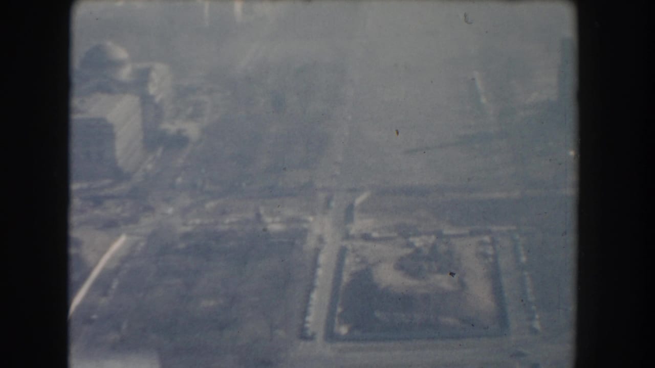 1960 Washington, DC aerial frame showing a hazy domed building area with roads and open civic landscape below.