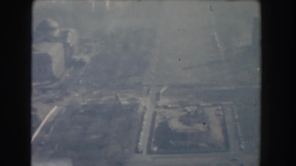 1960 Washington, DC aerial frame showing a hazy domed building area with roads and open civic landscape below.
