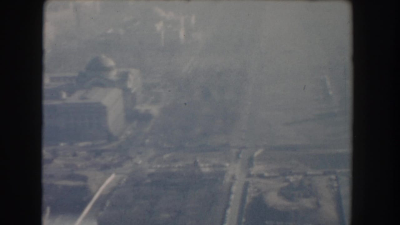 Soft aerial view of a domed structure area with roads, haze, and distant buildings.