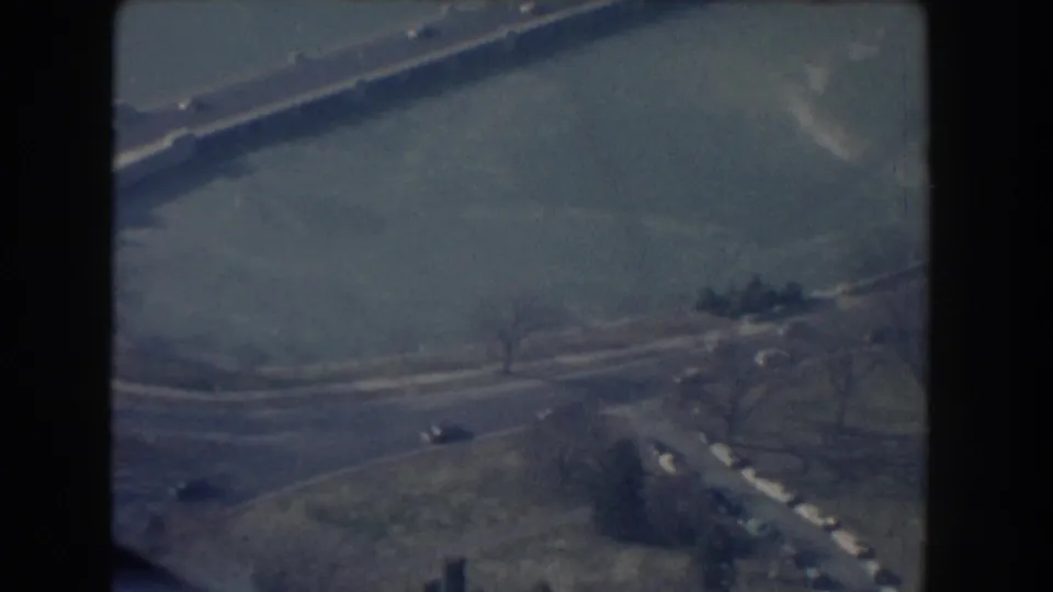 1960 Washington, DC aerial frame looking down over a broad road, pale water or paved expanse, lawns, and small cars.