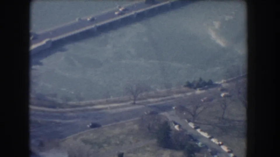 Late-frame 1960 Washington, DC aerial view with roadways, small cars, grass, bare trees, and a pale open expanse.