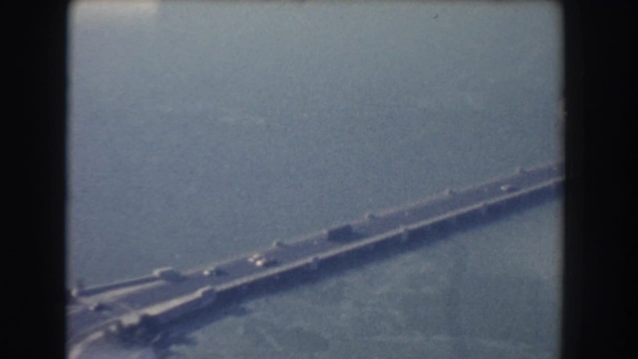 1960 Washington DC aerial home-movie frame showing a long bridge over water with small cars and hazy focus.