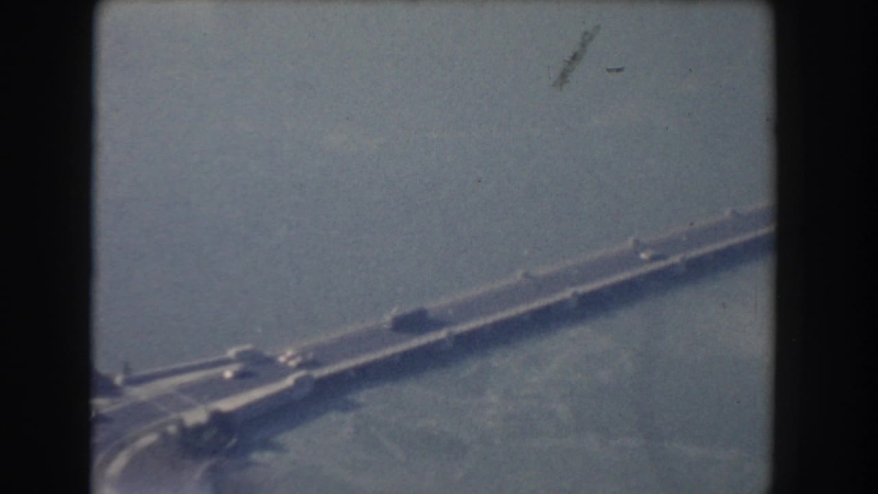 Aerial view of the bridge continuing across water with traffic and soft haze.