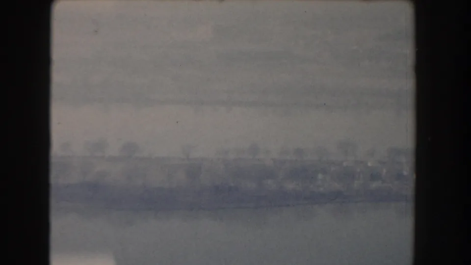 1960 Washington DC aerial home-movie frame showing water, a hazy shoreline, bare trees, and low buildings.