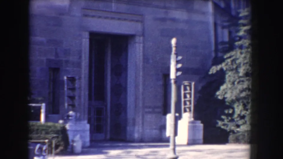 Close Washington DC 8mm exterior of a gray stone building, traffic signal, paved foreground, shrubs, and green tree.
