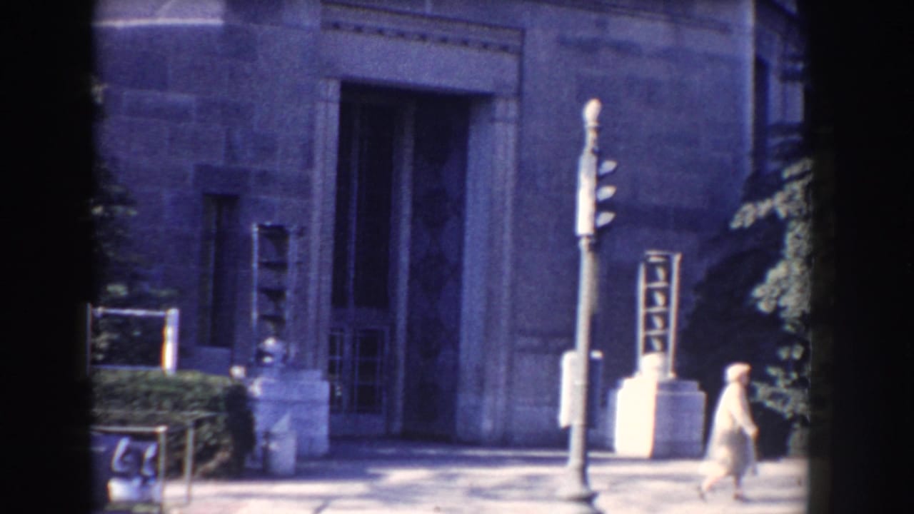 1960 Washington, DC frame with a woman walking past the FBI building entrance and traffic signal.