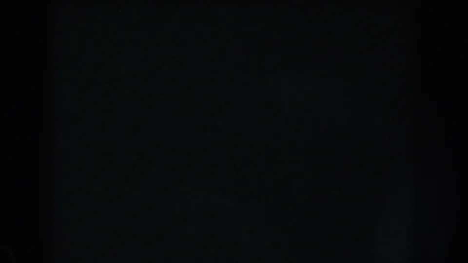 Dark 8mm home-movie frame with almost no legible subject, showing subtle grain and a central shadowed division.