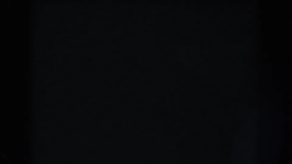 Underexposed home-movie frame from the reel, with black film surface, slight grain, and barely visible border shadows.