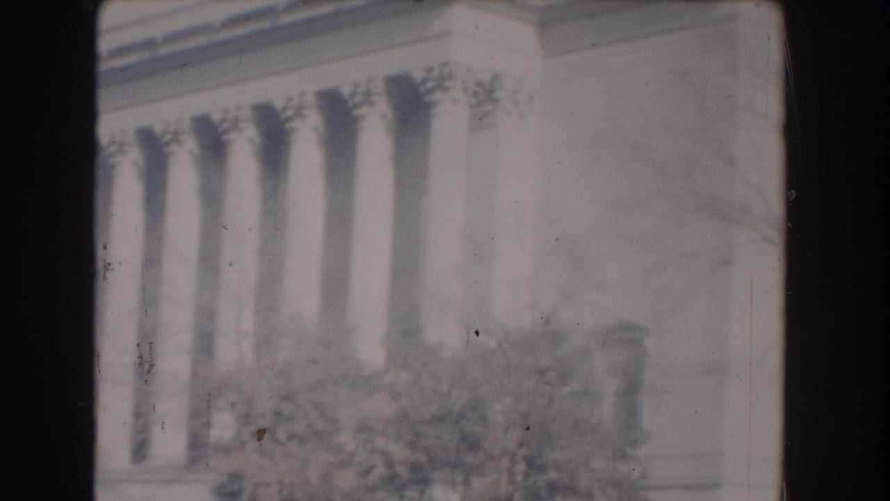 1960 Washington, DC home-movie frame showing pale Jefferson Memorial columns behind shrubs and soft film wear.