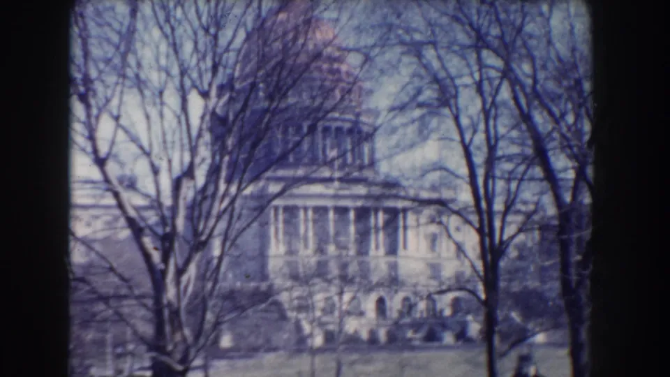 Blue-shifted 1960 home-movie frame of the U.S. Capitol seen through trees, with lawn visible near the bottom.