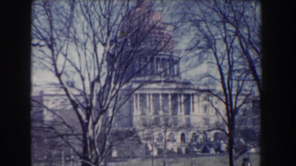Late-frame 1960 Washington, DC view of the Capitol through trees, with visible 8mm grain and dark gate edges.